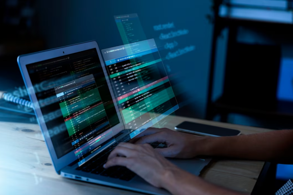 Hands typing on a laptop keyboard with holographic code projections in a dimly lit room.